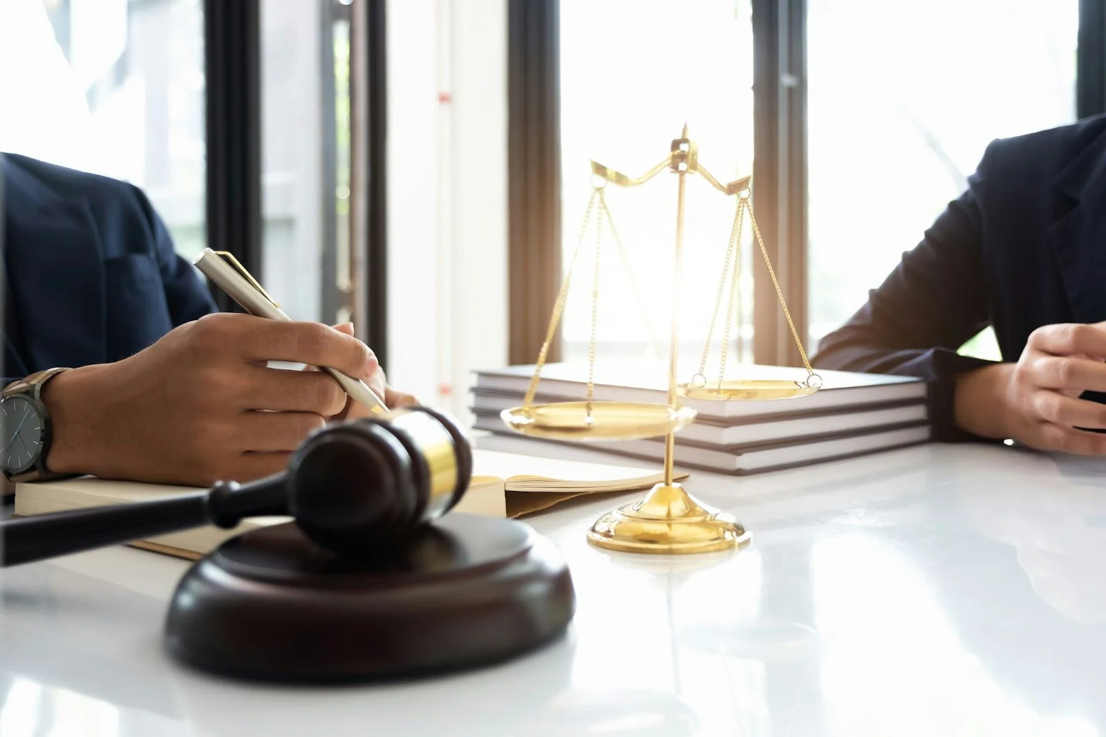 Close-up of a gavel, golden scales of justice, and legal books on a white table.